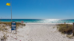 A sandy beach path leading to the ocean with a flag, a signboard, and a wooden fence. - Summersalt 1 Bedroom Condo by RedAwning (Santa Rosa Beach)