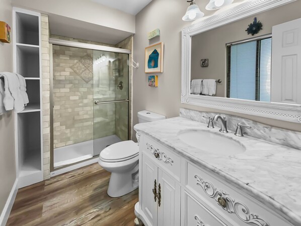 A modern bathroom with a glass-enclosed shower, a white toilet, and a marble vanity with a large mirror.