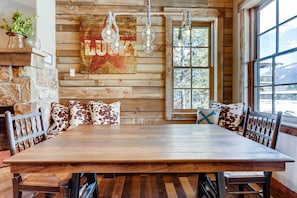 A rustic dining area with a wooden table, benches, and a stone wall.