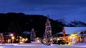 Una piazza innevata con alberi di Natale e palazzi illuminati.