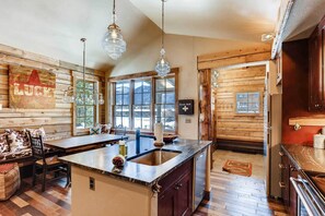 Una cocina con paredes de madera, una isla grande con un fregadero e iluminación colgante.