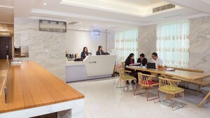 A reception area with a marble wall, a reception desk, and a seating area with chairs and a table. - San Tung Fong Commercial Inn South Wing (Macau)