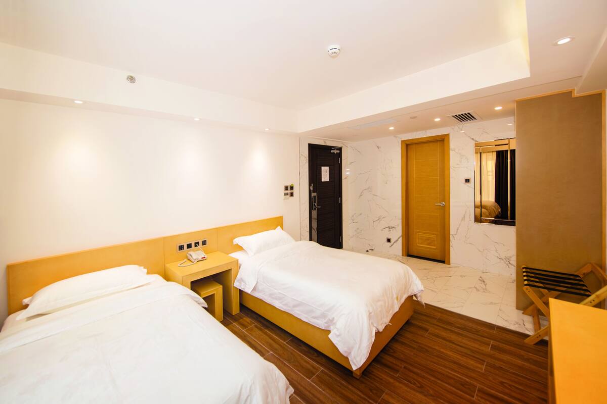 Camera d'albergo con due letti, una testiera in legno, un comodino con il telefono e una porta che dà su un bagno.