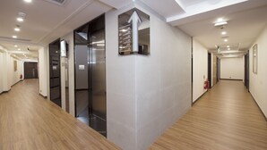 A modern hotel corridor with wooden flooring, a central elevator, and a fire extinguisher on the right wall. - San Tung Fong Commercial Inn South Wing (Macau)