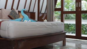 Ein Schlafzimmer mit einem Holzbettrahmen, einer weißen Matratze und Blick ins Grüne durch eine Glastür.