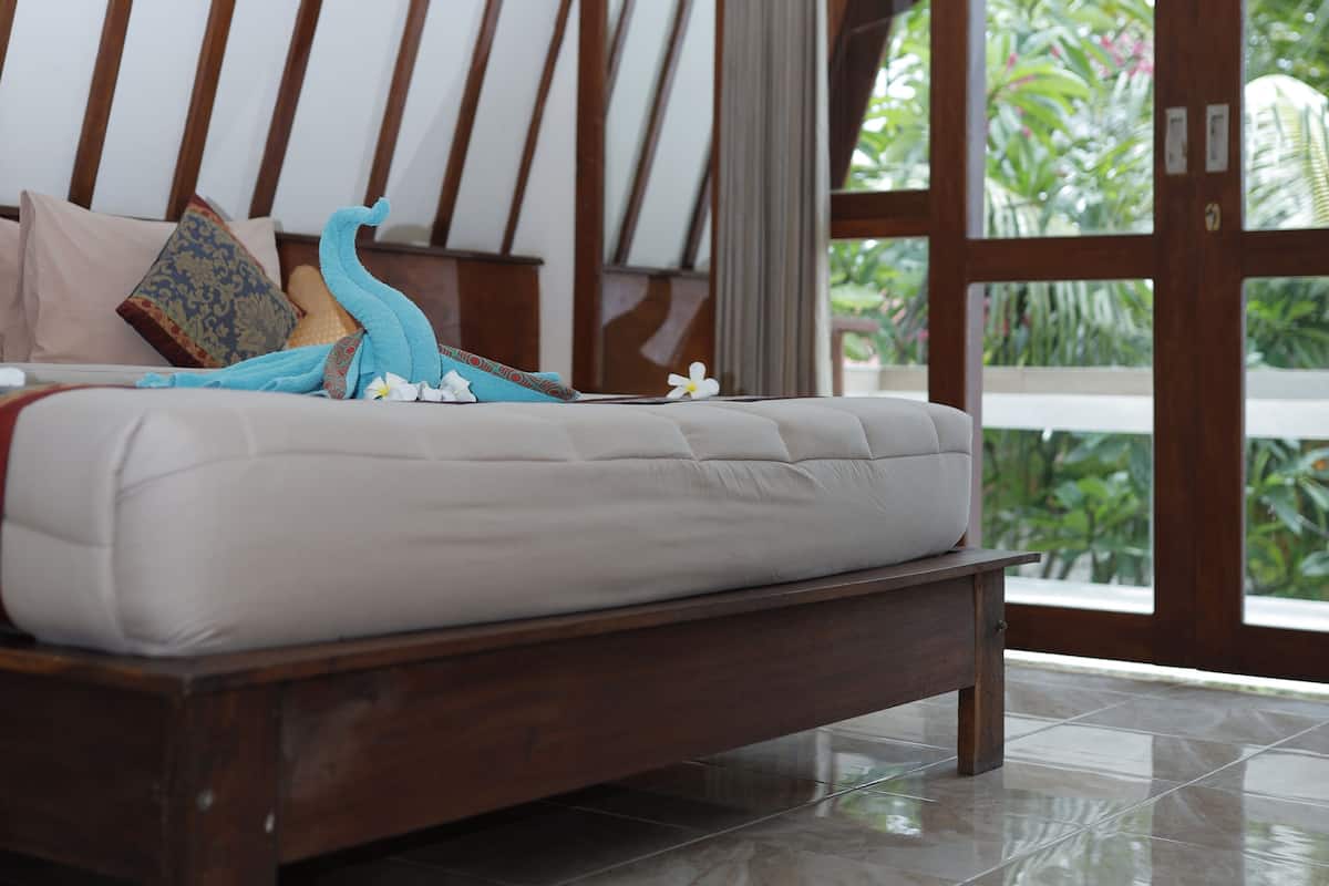 Une chambre à coucher avec un cadre de lit en bois, un matelas blanc et une vue sur la verdure, visible à travers une porte vitrée.