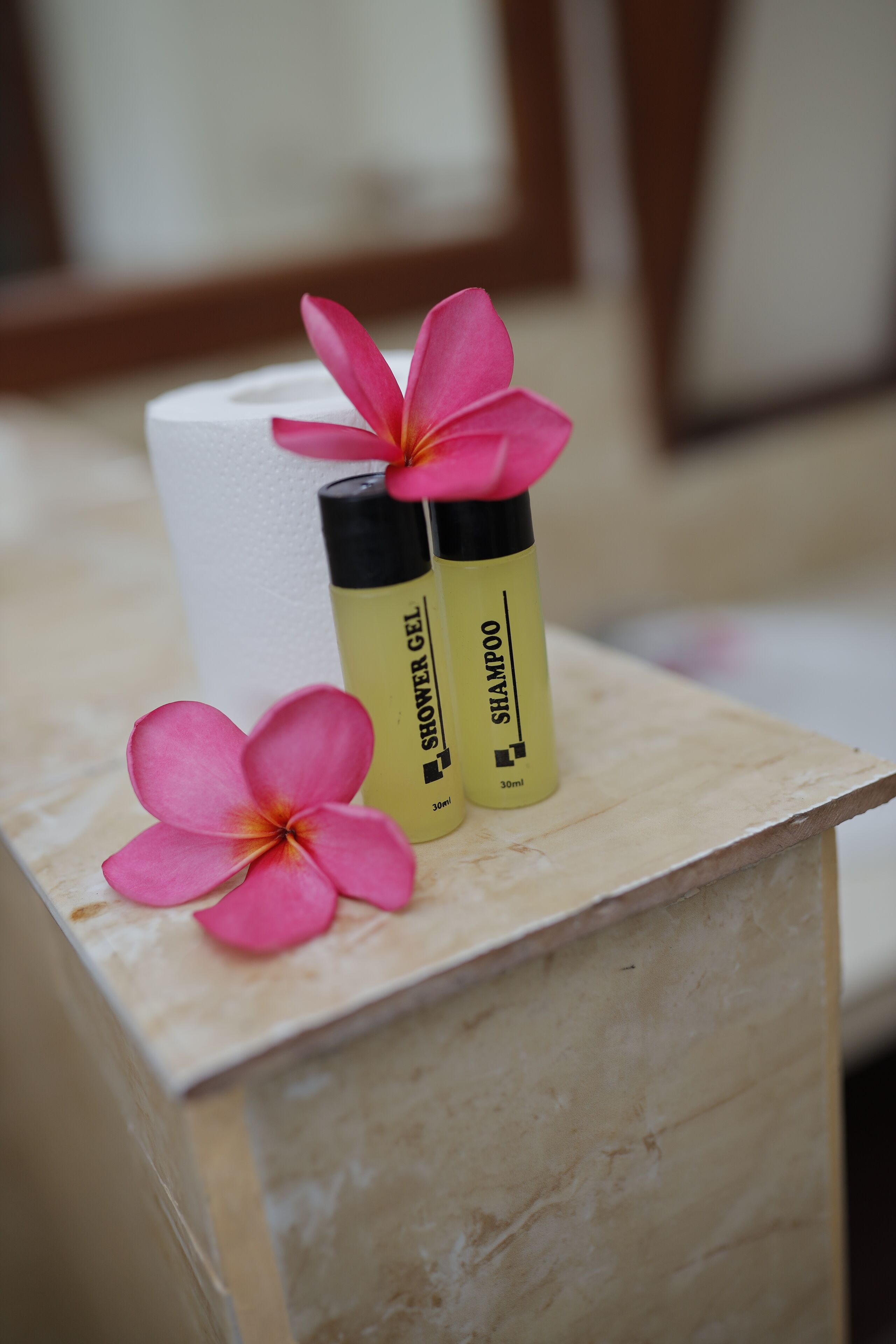 A wooden box with two bottles of shower gel and shampoo, and a pink flower on top.