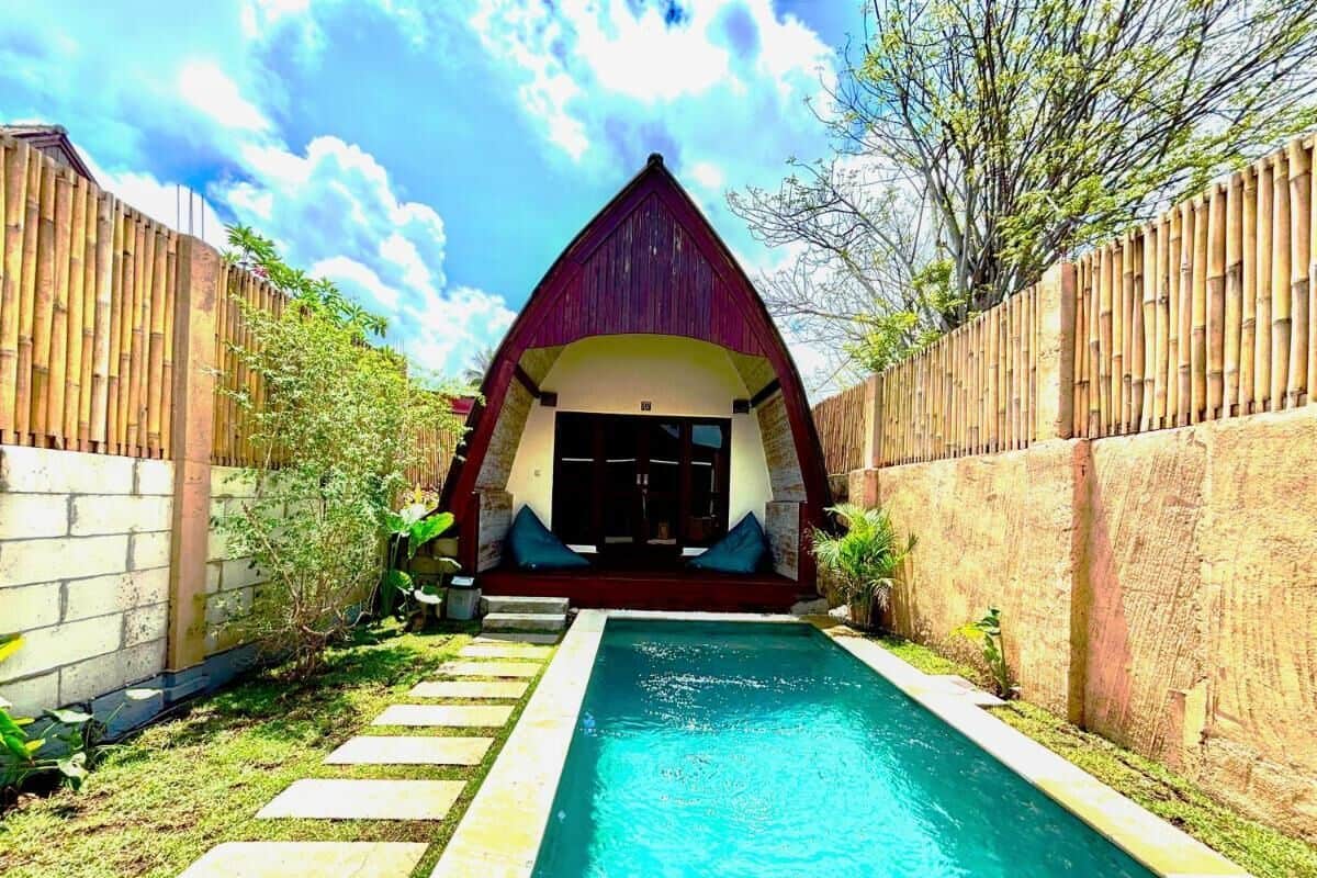 Une piscine bordée de chaque côté par une clôture en bois, qui mène à un bâtiment doté d’un toit rouge et d’une porte.