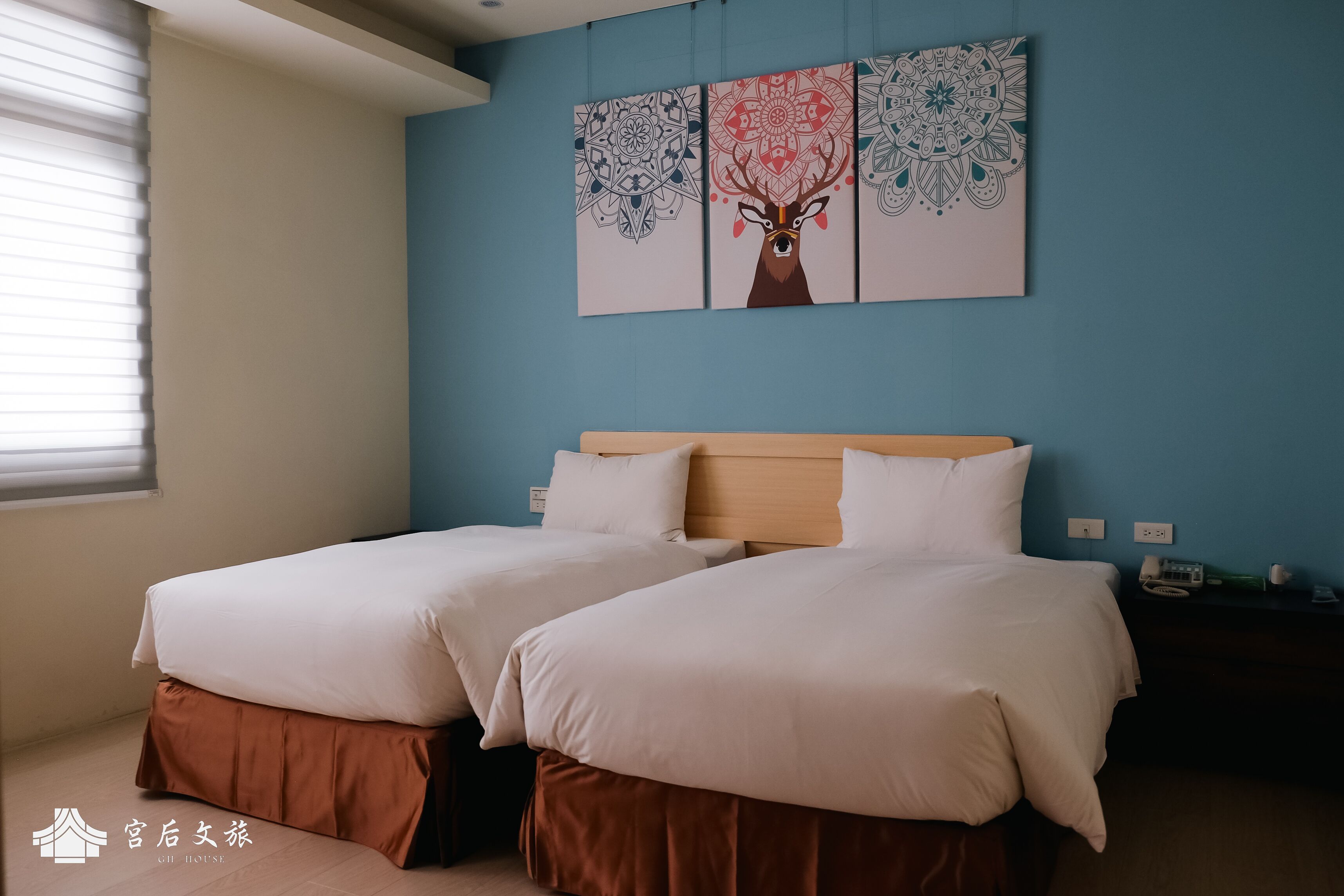 Une chambre d’hôtel avec deux lits, un mur d’accent bleu et un élément décoratif mural.