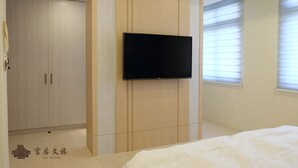 A bedroom with a bed, a wardrobe, a television mounted on the wall, and a window with blinds.