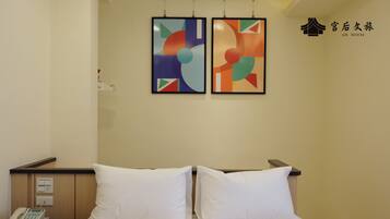 A hotel room with a bed, a nightstand with a phone, and two abstract paintings on the wall.