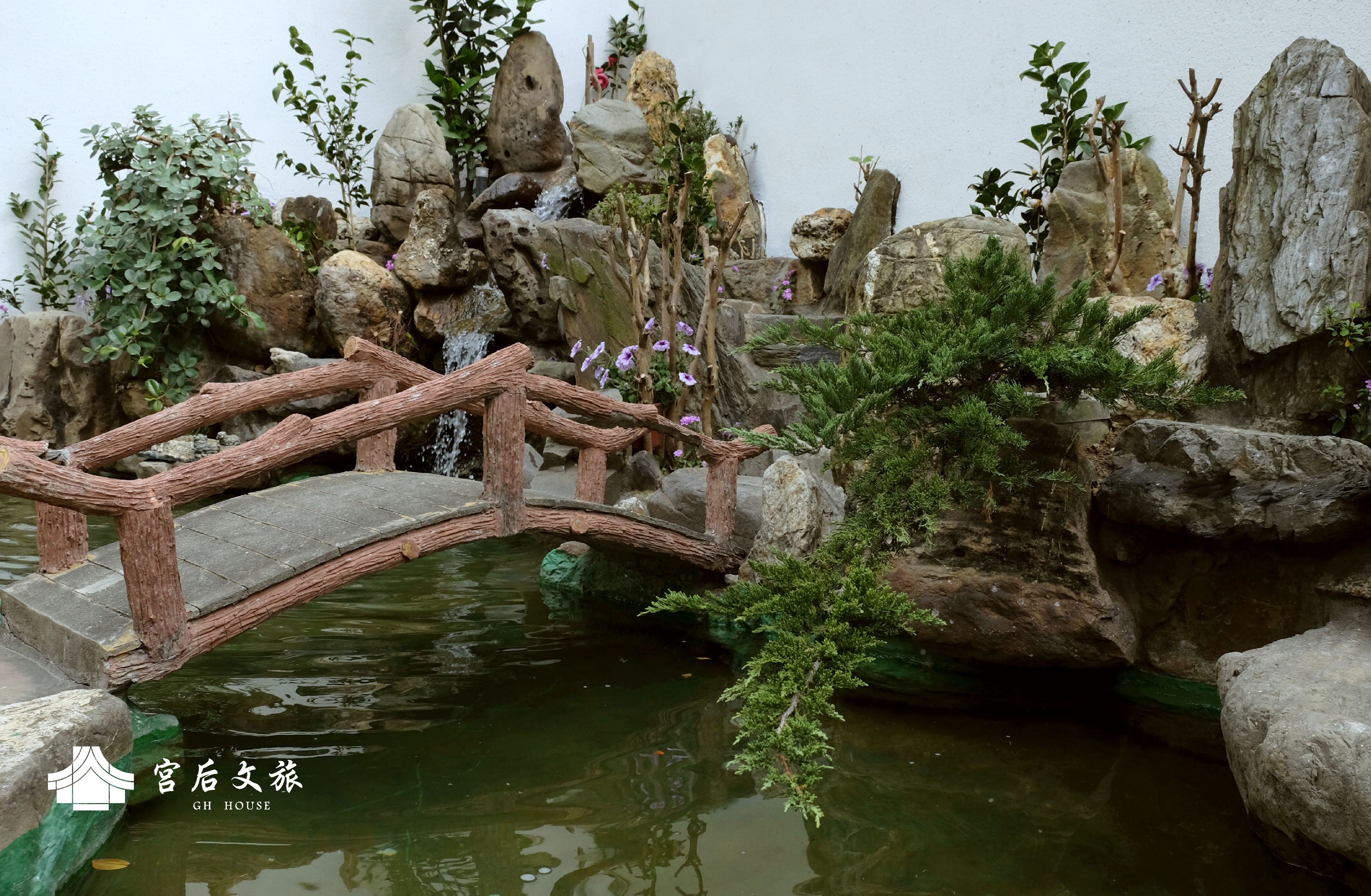 Un puente de madera sobre un estanque con rocas y vegetación.
