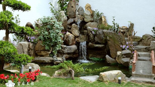A rock garden with a small waterfall, surrounded by various plants and flowers.