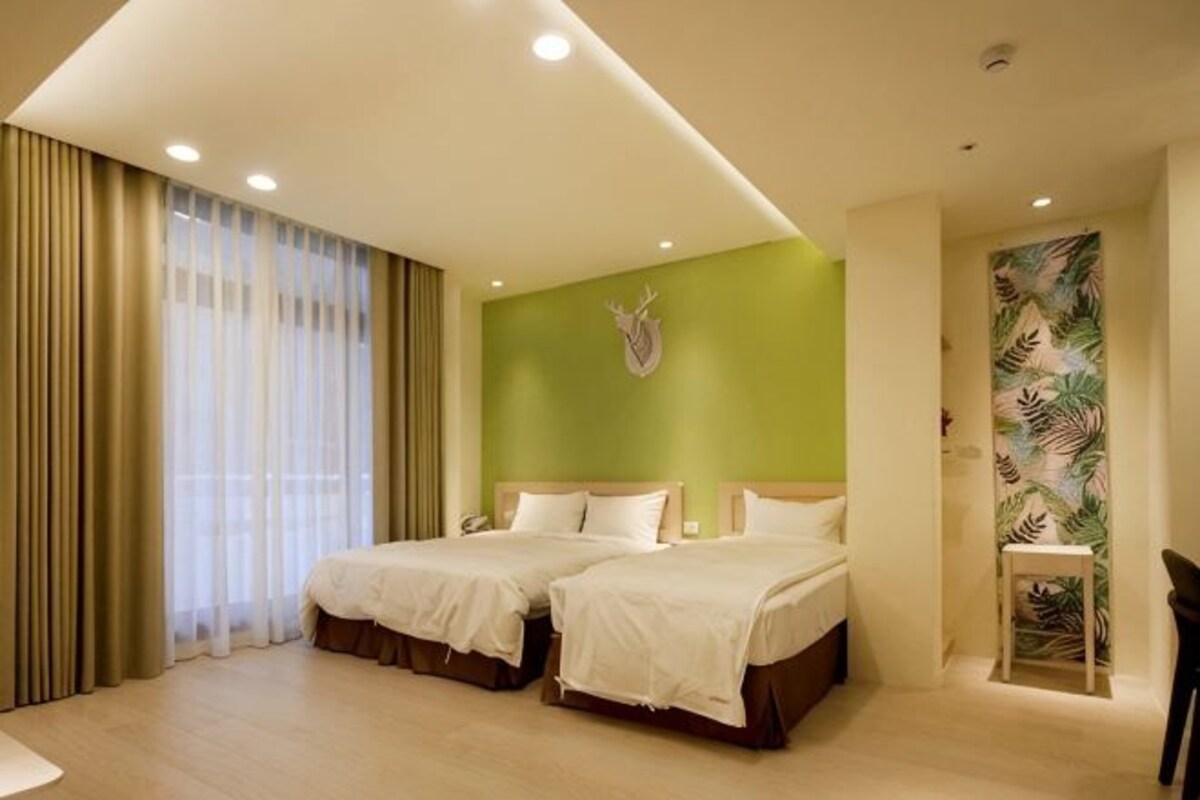 A hotel room with two beds, a green accent wall, and a tropical leaf wallpaper.