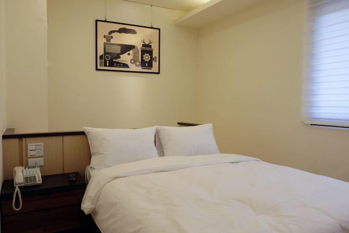 A hotel room with a bed, a bedside phone, and a wall-mounted artwork.