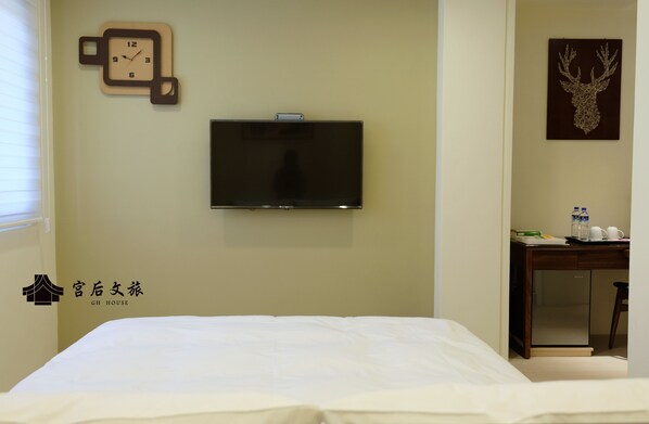 A hotel room with a bed, a flat-screen TV mounted on the wall, a clock, a deer head artwork, and a desk with a refrigerator. - Gh House (Lukang)