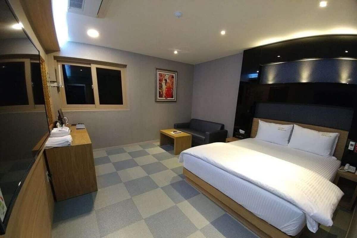 A hotel room with a large bed, a desk, a chair, a small table, and a window.