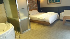 A hotel room with a bed, a white sofa, a painting on the wall, and a bathroom with a bathtub and sink.