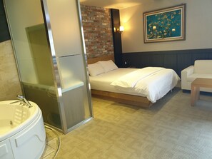 A hotel room with a bed, a white sofa, a painting on the wall, and a bathroom with a bathtub and sink.