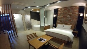 A hotel room with a bed, a wooden table with chairs, a small desk, a bathtub, and a brick wall. - Khan Hotel (Daegu)