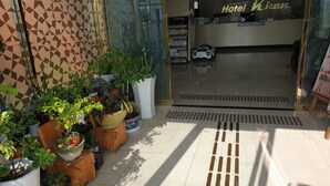 A hotel entrance with a geometric patterned wall, potted plants, and a reception desk with a car model.