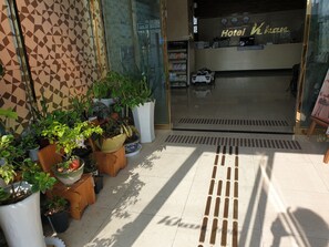 A hotel entrance with a geometric patterned wall, potted plants, and a reception desk with a car model. - Khan Hotel (Daegu)