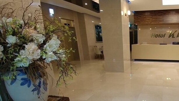 A hotel reception area with a modern design, a reception desk, and a decorative floral arrangement. - Khan Hotel (Daegu)