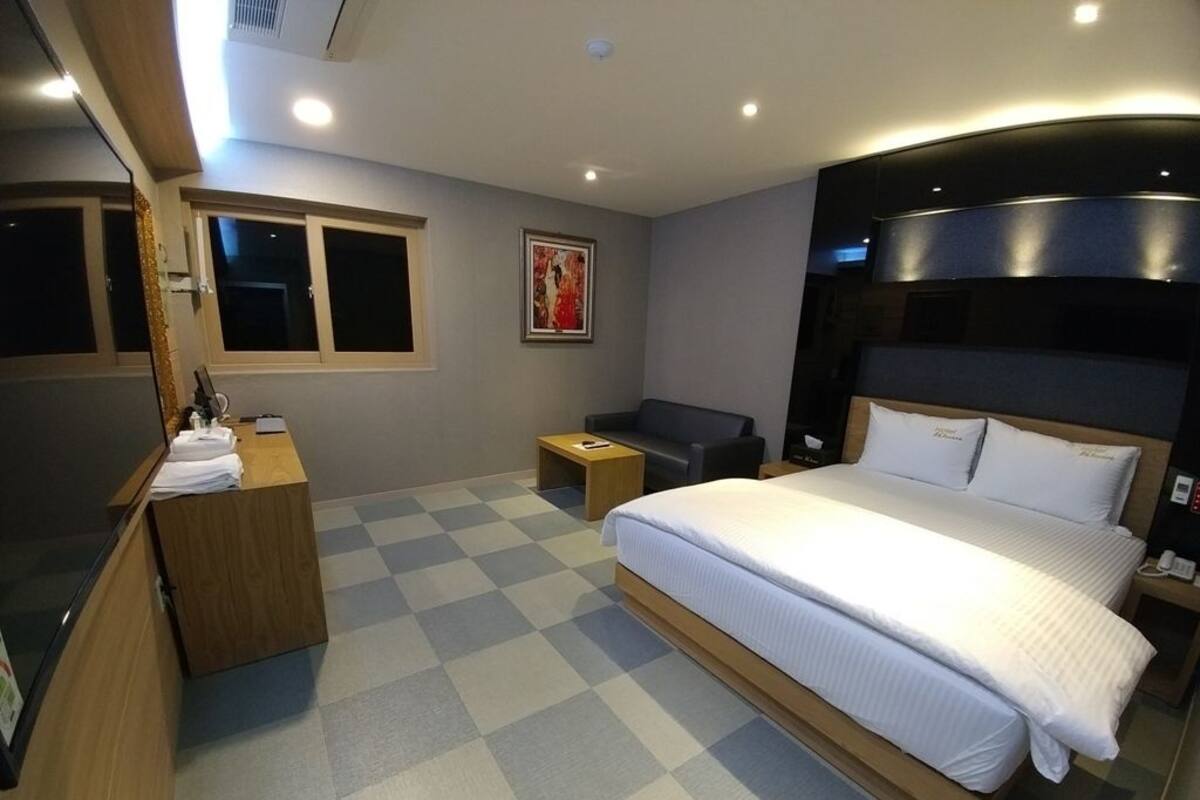 A hotel room with a large bed, a desk with a chair, a small table, and a window.