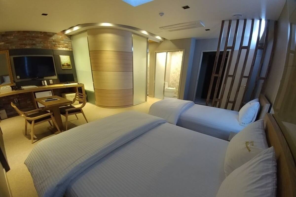 A hotel room with a large bed, a desk with a chair, a television, and a sliding door leading to a bathroom.