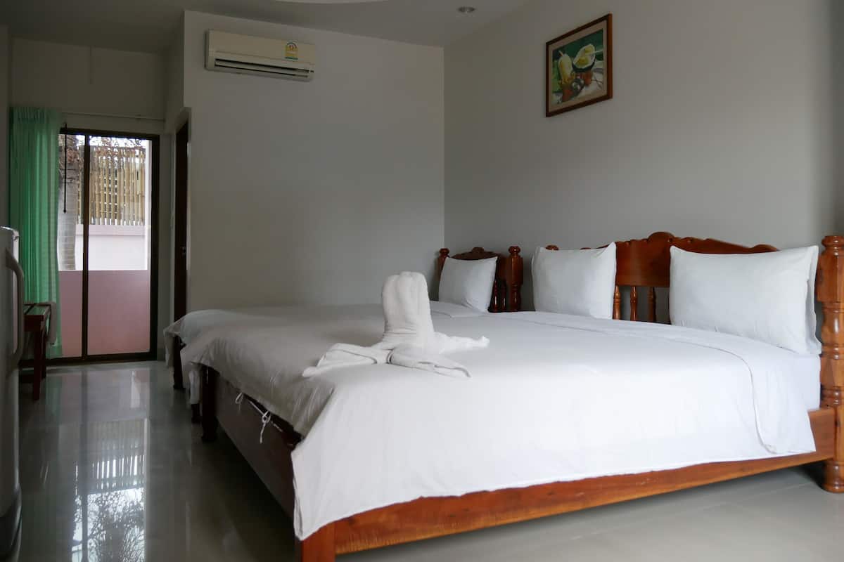 A hotel room with a large bed, a wooden headboard, a painting on the wall, and an air conditioning unit.