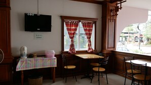 A dining area with a table and chairs, a television mounted on the wall, and a window with curtains. - Dalha Renovtel Hotel (Nakhon Phanom)