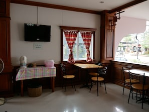 A dining area with a table and chairs, a television mounted on the wall, and a window with curtains. - Dalha Renovtel Hotel (Nakhon Phanom)