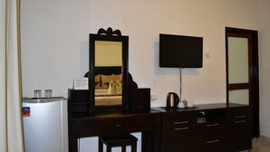 A hotel room with a bed, a desk, a television, a mirror, and a refrigerator. - Meisya Cottage (Gili Trawangan)