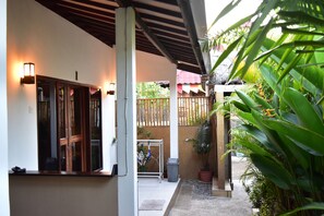 A covered outdoor area with a wooden bench, a trash bin, and potted plants. - Meisya Cottage (Gili Trawangan)