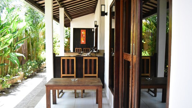 A covered outdoor dining area with a wooden table and chairs, a sink, and a mirror. - Meisya Cottage (Gili Trawangan)