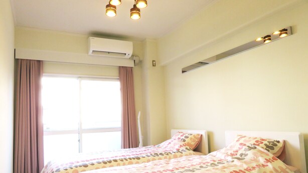 Ein Hotelzimmer mit zwei Betten, einem Fenster mit Vorhängen, einer Klimaanlage und einer Deckenleuchte.