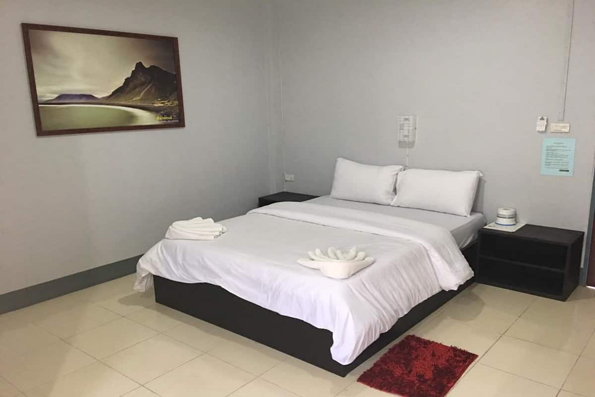 Una cama bien tendida con sábanas y toallas blancas, una alfombra roja y un cuadro de un paisaje en la pared.