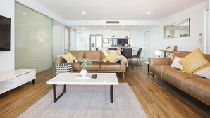 A modern living room with a brown leather sofa, a white coffee table, and a TV mounted on the wall.