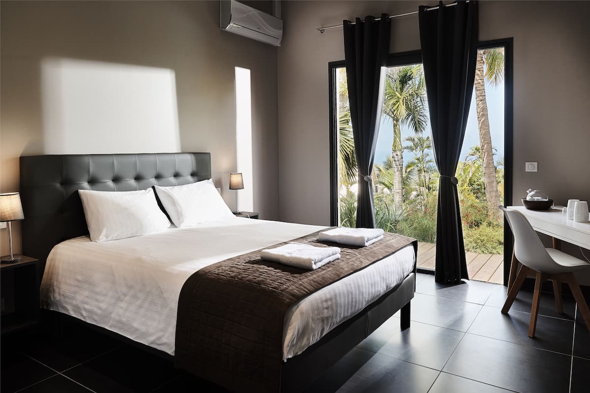 Habitación de hotel moderna con una cama grande, un escritorio y vistas a palmeras a través del ventanal.