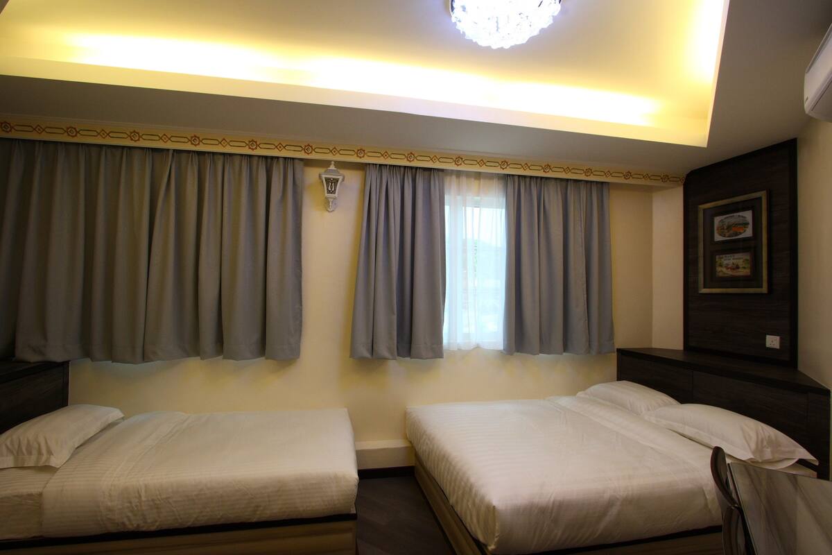A hotel room with two single beds, a nightstand, a lamp, and a framed picture on the wall.