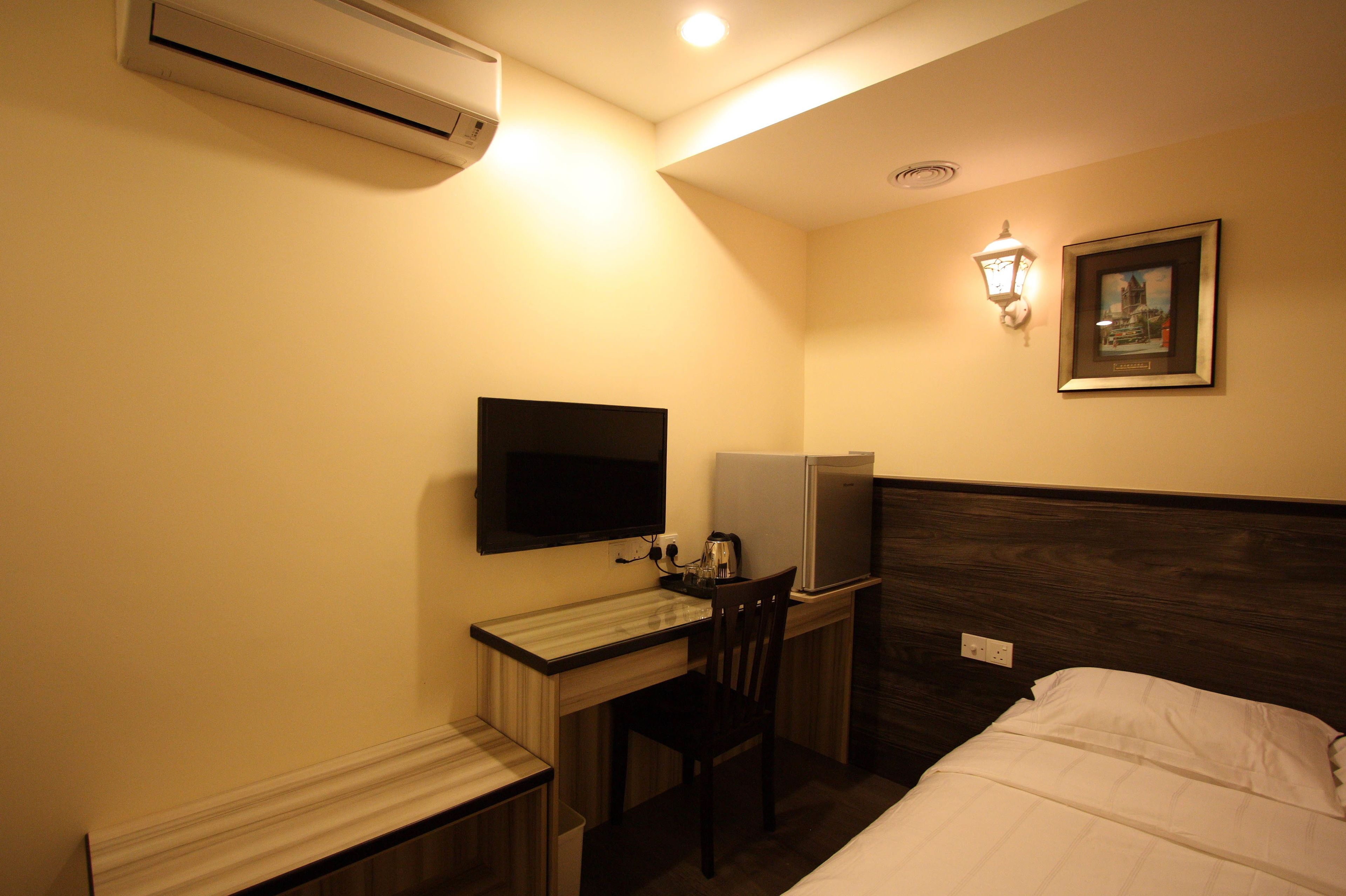 A hotel room with a bed, a desk, a chair, a television, a refrigerator, and a wall-mounted air conditioner.