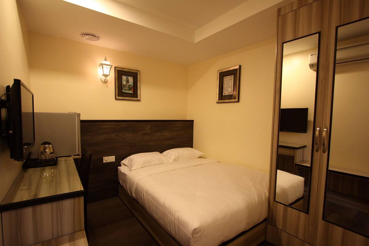 A hotel room with a bed, a bedside table with a lamp, a mirror, and two framed pictures on the wall.