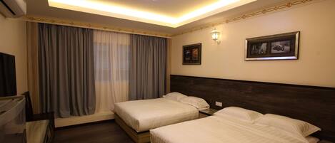 A hotel room with two beds, a ceiling light, a TV, and a window with curtains.