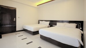 Une chambre d’hôtel avec deux lits, une porte en bois sombre et un sol carrelé.
