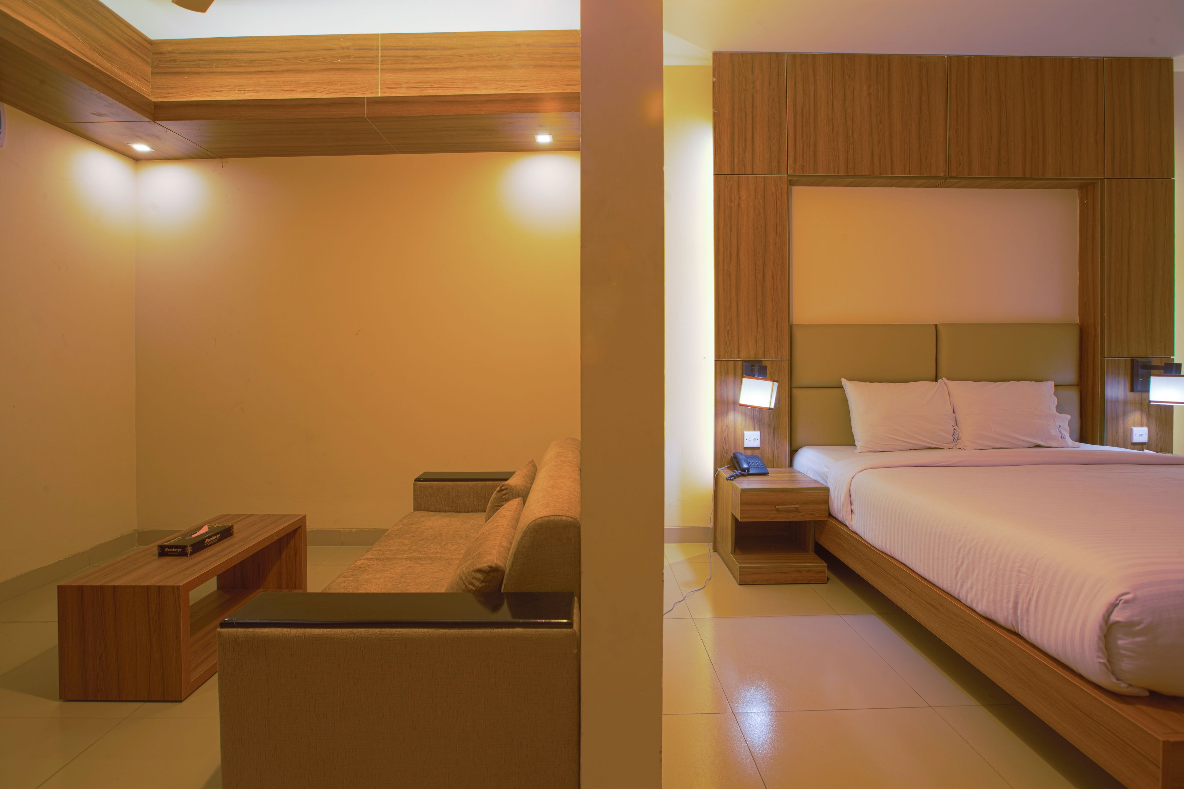 A modern bedroom with a wooden headboard, a bed with white bedding, a nightstand with a lamp, and a small wooden bench.