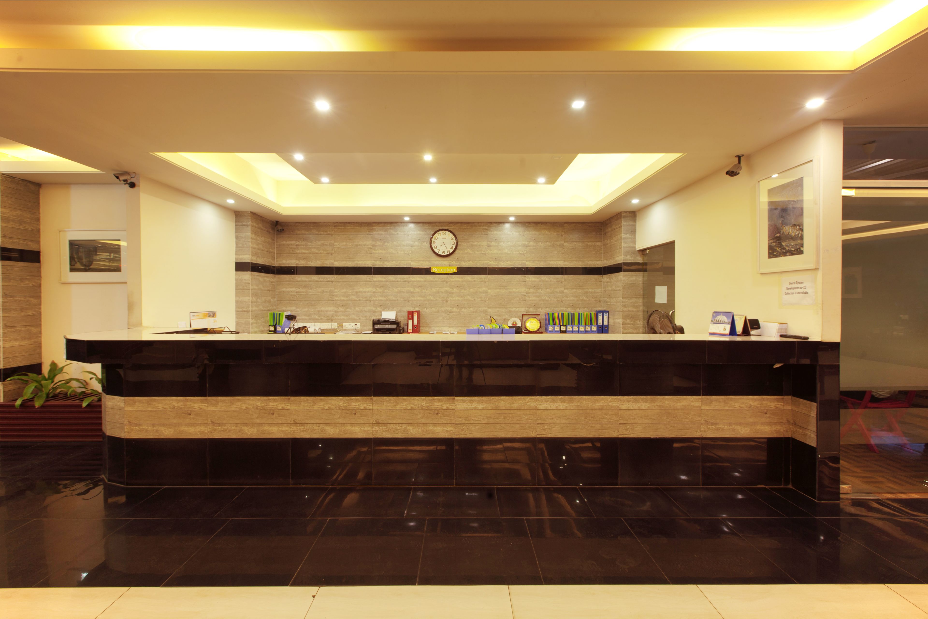 A reception area with a black reception desk, a clock on the wall, and a plant to the left.