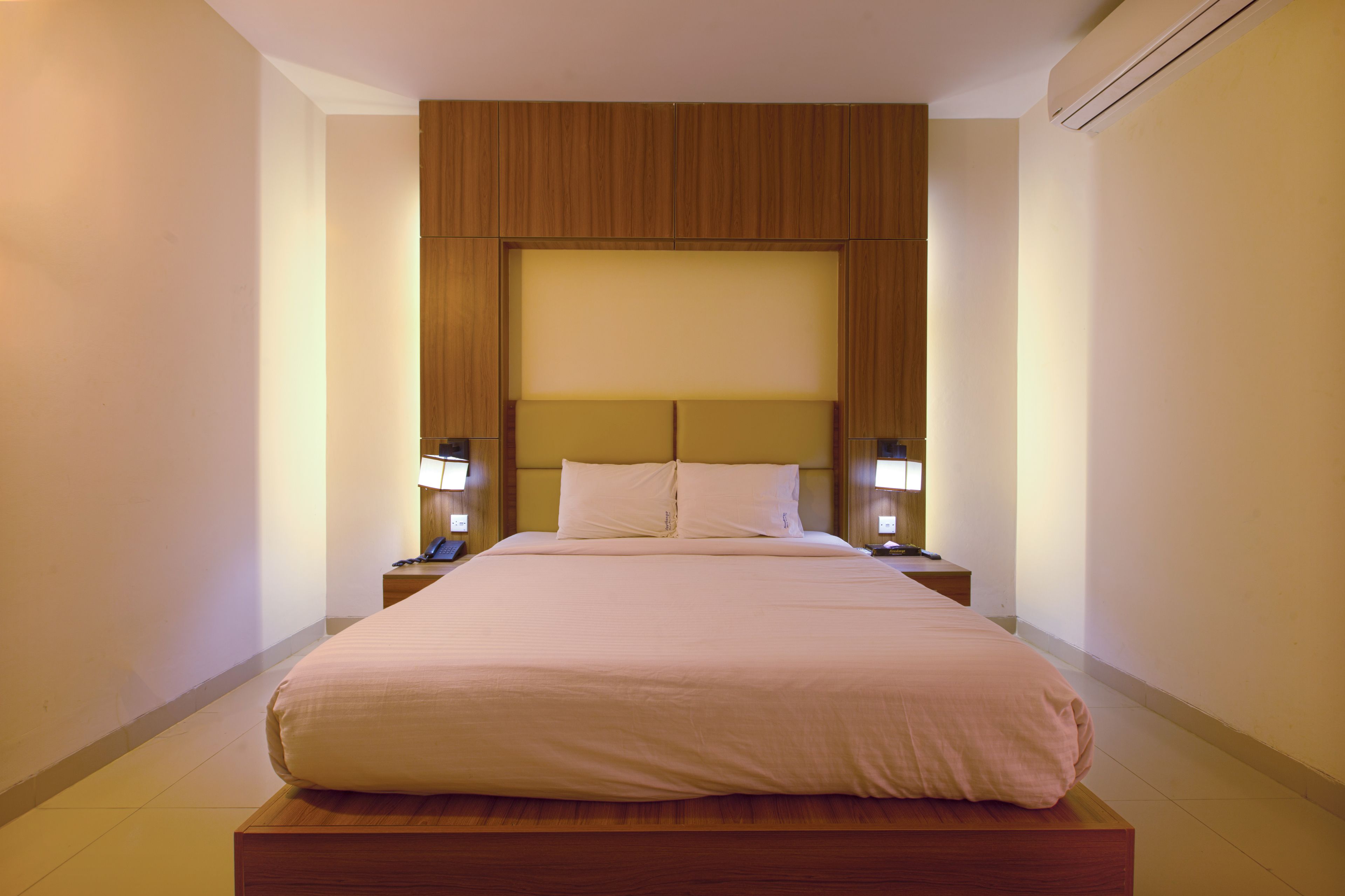 A hotel room with a large bed, wooden headboard, bedside lamps, and a nightstand.