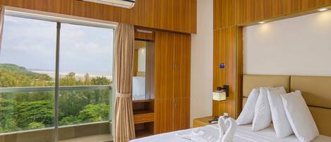 A hotel room with a large bed, a view of the outdoors, a wooden wardrobe, and a ceiling fan.