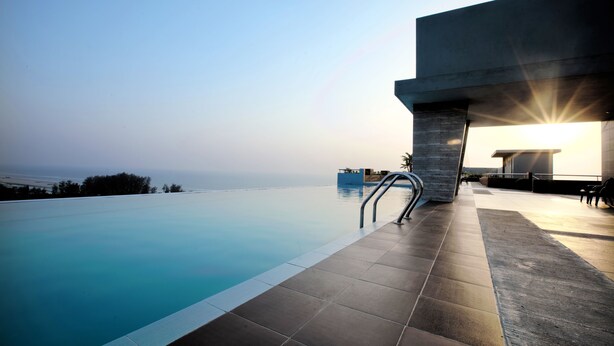 Une piscine à débordement moderne, avec une eau d’un bleu cristallin, une structure en béton et une vue sur la mer.