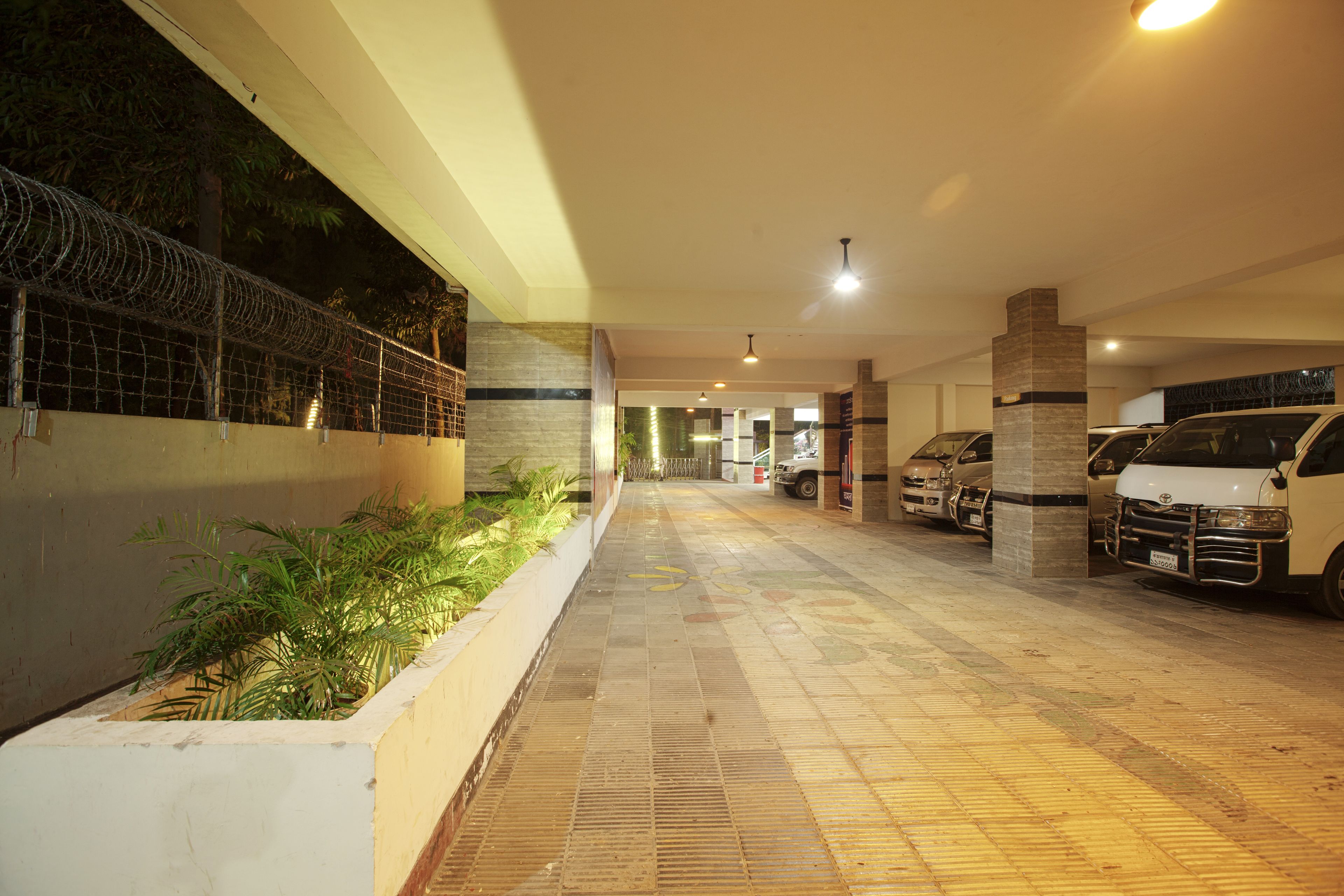 A parking area with a tiled floor, a white van, and a security fence.